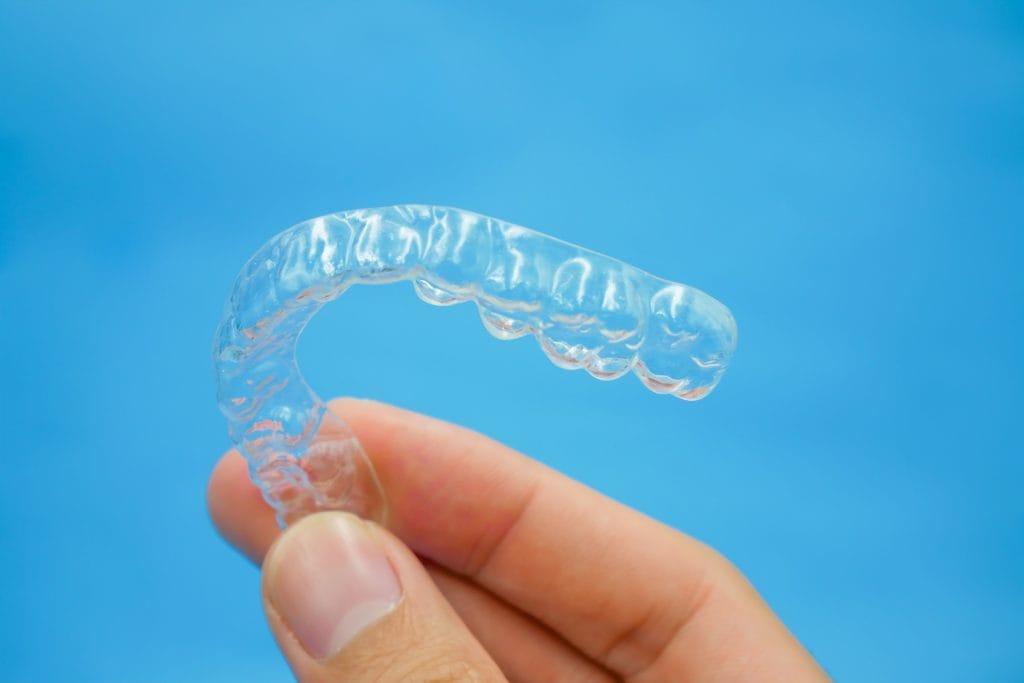 hand holding clear plastic retainer teeth that isolated on blue
